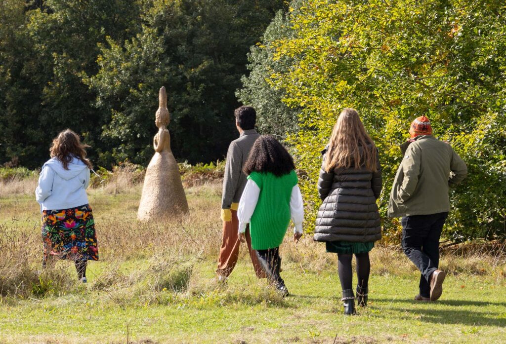 A group of five young people seen from behind walking through a field towards an outdoor sculpture at Sainsbury Centre Norwich Sculpture Park.
