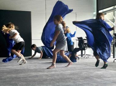 A group of school children dancing with blue scarves in an art gallery