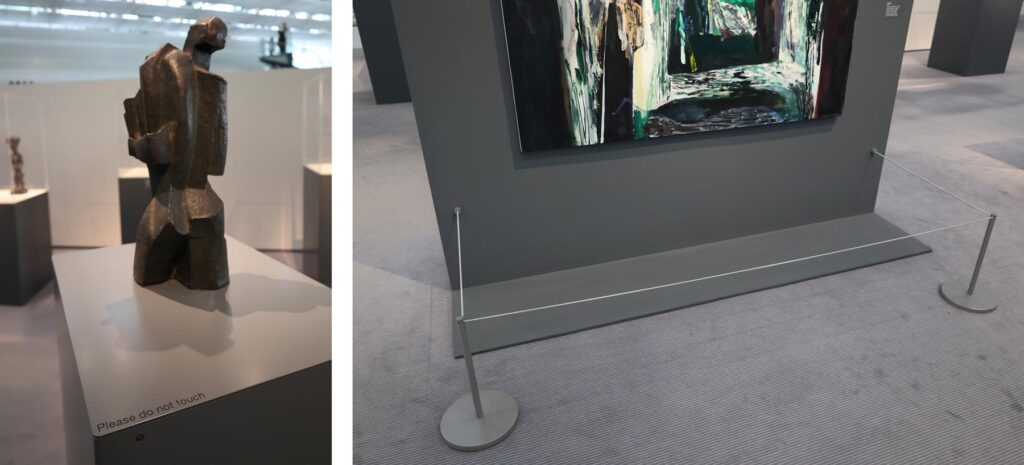 Photo of an artwork in a museum with a sign next to it saying Please do not touch. A painting in the art museum with low barriers in front of it to stop visitors from going to close.