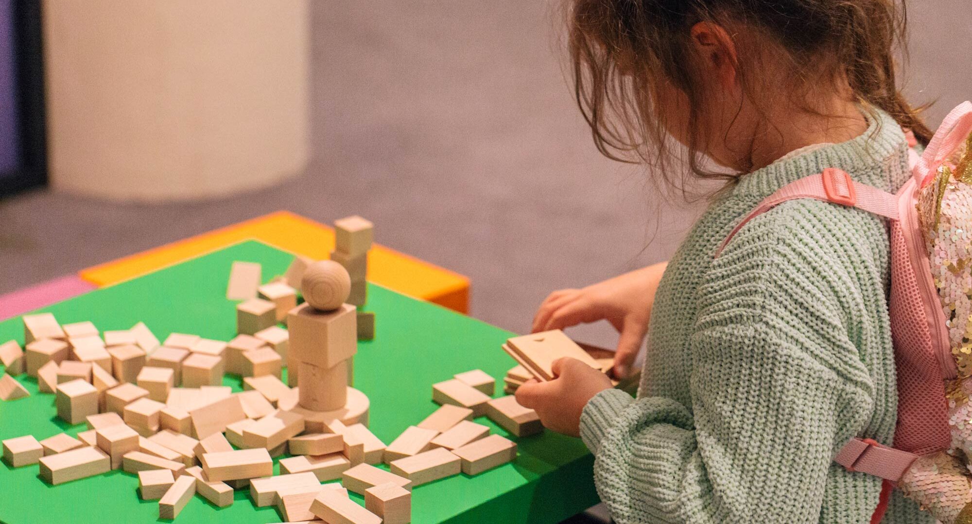 A young girl seen from behind playing a table top board game made from small wooden blocks